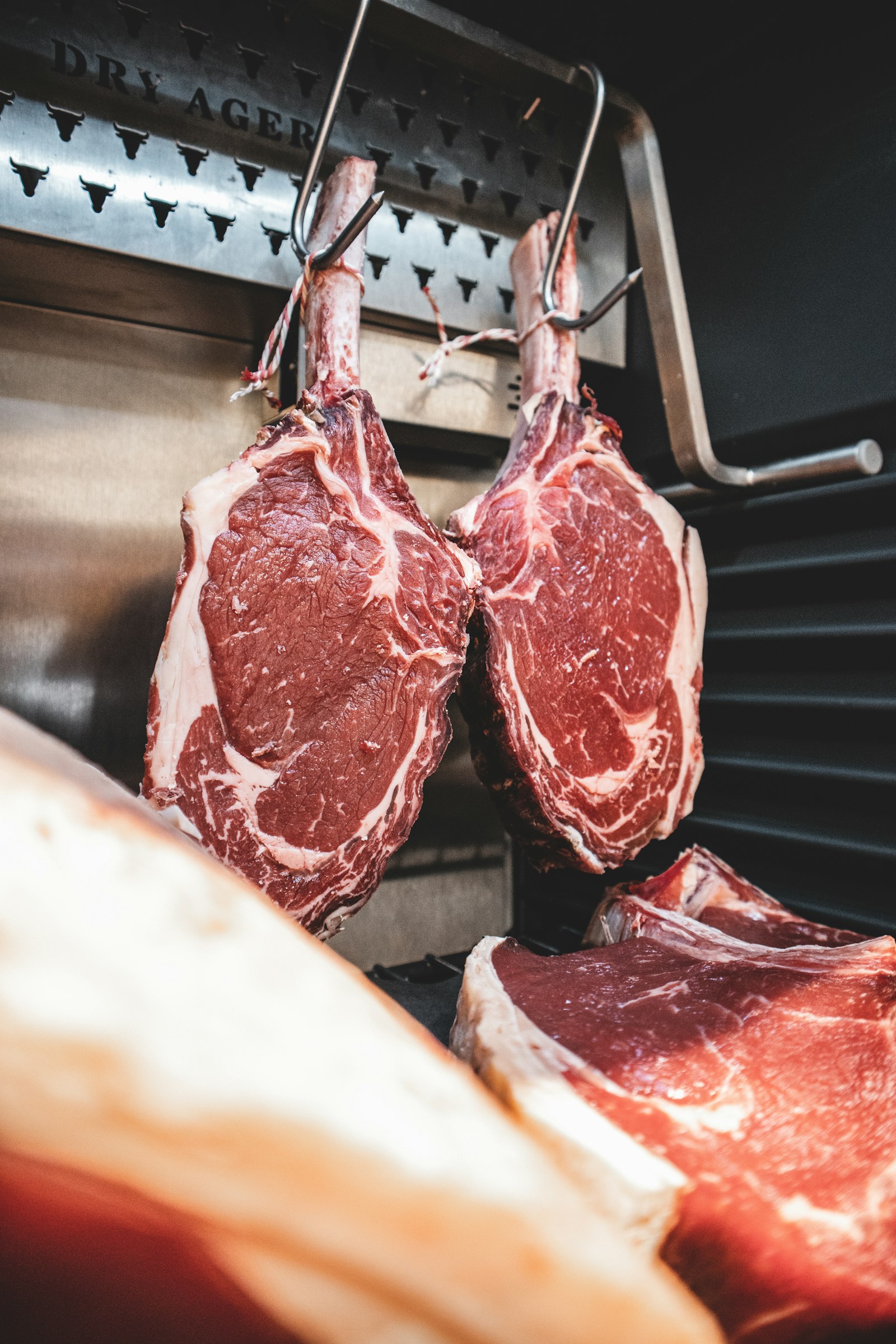 Cuts of beef hanging from steel hooks inside a dry-aging cabinet
